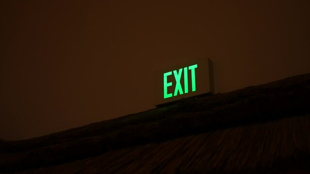 Camera pans to a light green lit exit sign in building