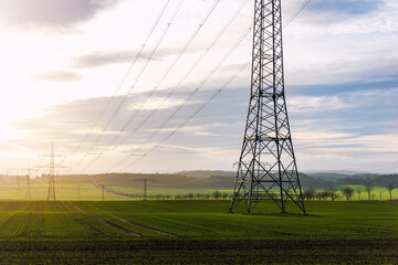 Scenic view of electricity pylons stretching across green fields warm sunset sky background....