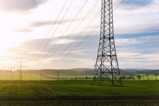 Scenic view of electricity pylons stretching across green fields warm sunset sky background. Electric power supply high voltage metal tower in Europe