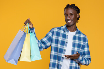 Smiling Young Black Man Demonstrating Bright Shopping Bags In His Hand