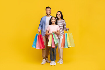 Happy caucasian family of three holding bright shopping bags