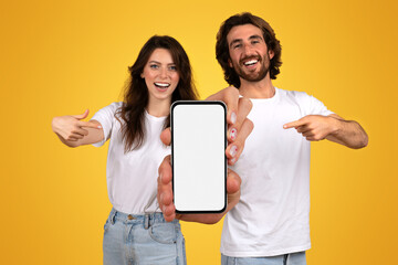 Enthusiastic young couple in white t-shirts presenting a smartphone with a blank screen
