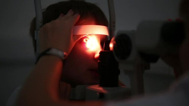 Oculist is inspecting mans eyes by the slit lamp at dark.