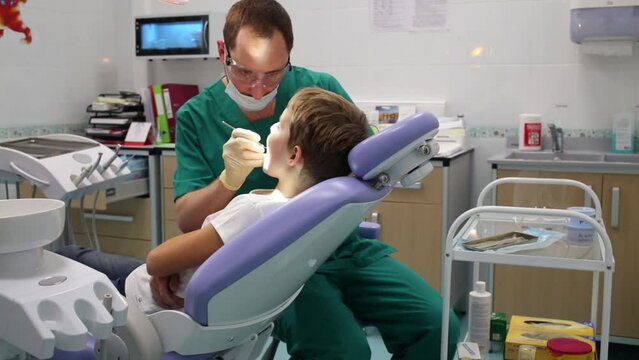 Dentist is inspecting little boys teeth near dental drill at Children clinic