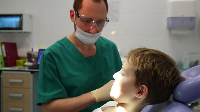 Dentist is inspecting little boys teeth by mirror at Children clinic 