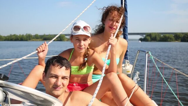 Man peeping out from hatch, girl and woman sitting on bow of yacht