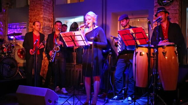 One blondy woman with a six musicians on the stage at musical bar.