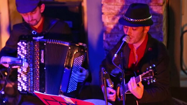 Men of band are playing with accordion and guitar at musical bar.