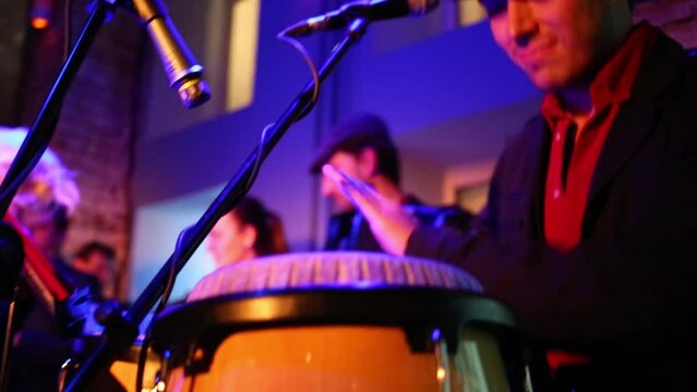 Musician of band in red shirt is playing on bongo at musical bar.