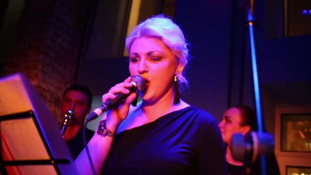 Beautiful blond girl of band is singing at musical bar.