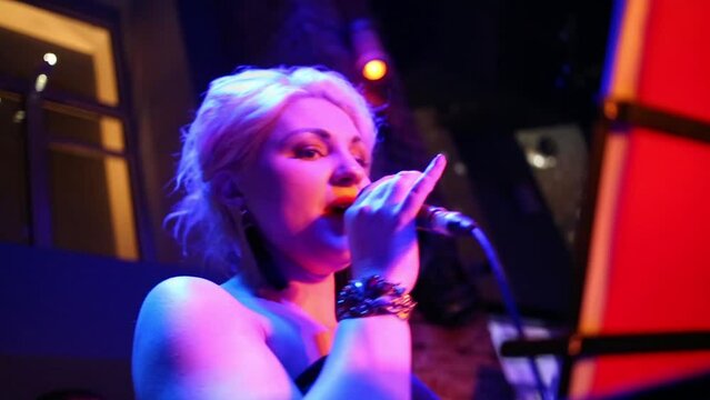 One beautiful blond woman of band is singing at musical bar.