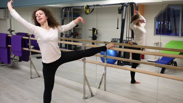 Woman put one leg on railing and bend hand to both legs in gym alone.