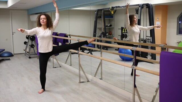 Woman put one leg on railing and squat on one leg with raised hands