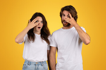 Shocked and curious couple with wide eyes covering one eye with their hands