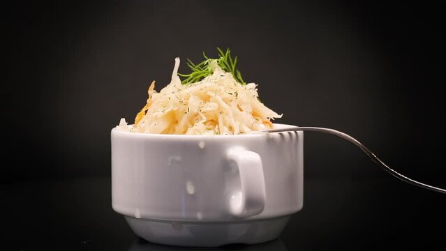 sauerkraut with carrots and spices in a white bowl isolated on a black background