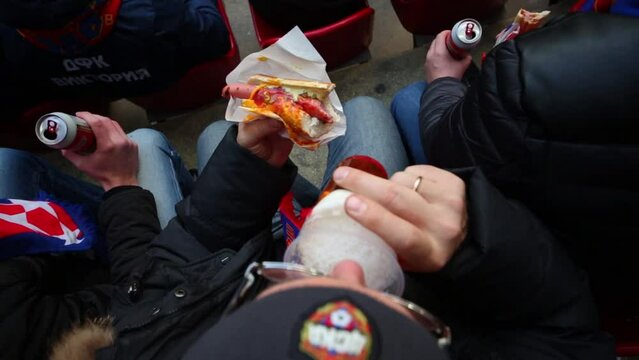 Men sit in grandstands, drinking beer and eating fast food during the match