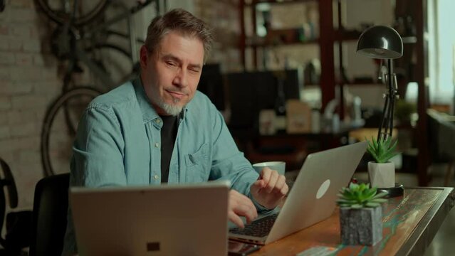Businessman using laptop computer managing small business online in home office. Happy, smiling man. Confident entrepreneur.