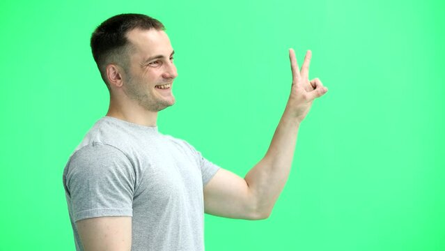 A man in a gray T-shirt, on a green background, close-up, shows a victory sign