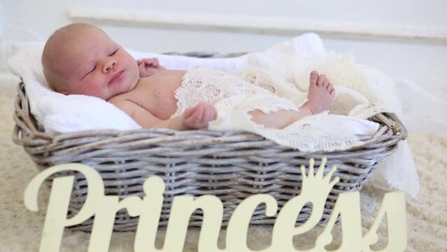 Little cute newborn baby is laying in wickered basket near sign