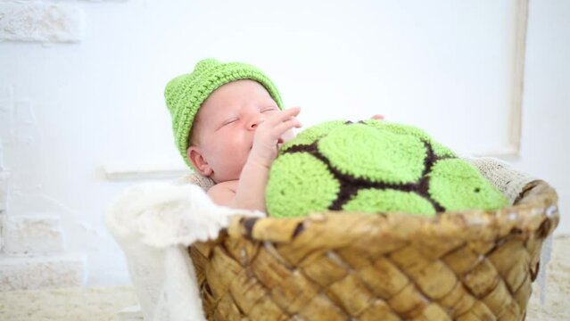 Little cute newborn baby is laying in wickered basket with green cap