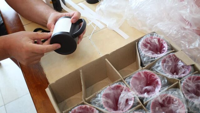 Man is sticking paper to th� black mug with a scotch tape.