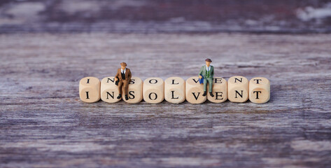 small miniature people in business suit sitting on wooden letters showing the word insolvent