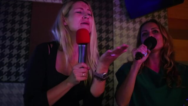 Two joyful women singing and dancing in karaoke club