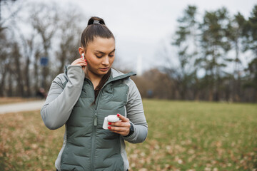 Woman Putting on Wireless Earbuds During an Outdoor Workout in the Park