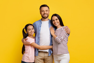Cheerful caucasian family of three posing together against yellow background
