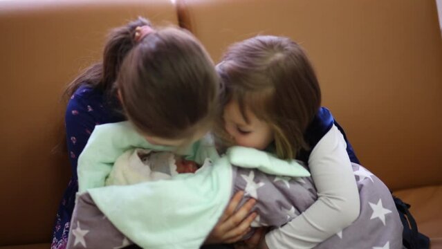 Two older sisters are caring and hugging newborn baby at the maternity clinic