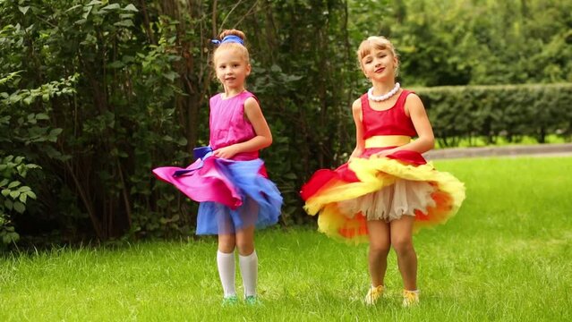Two girls in bright dresses dancing holding their skirts in park