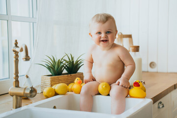 Cheerful baby in a kitchen sink bath with rubber ducks and lemons, happy moment