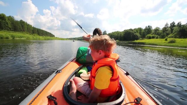 Boy sit and dress cap in canoe with rowing woman on river Tvertsa