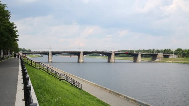 Embankment with unrecognizable walking people near bridge and river