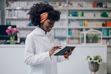 Portrait of a cheerful young African-American drugstore owner scrolling on a tablet.