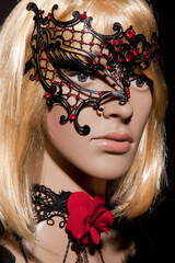 Mannequin with bright blond hair wearing a metallic half mask posing on a black background