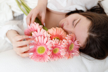 Beautiful woman with pink flowers on bed at home. St Valentine's Day. Women's day