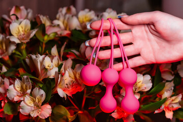 Woman's hand holds pink Kegel balls and Ben Wa balls on a background of flowers. Vaginal balls in a...