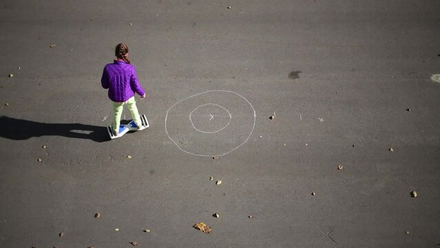 Girl on gyroscooter draws circles on the pavement with chalk