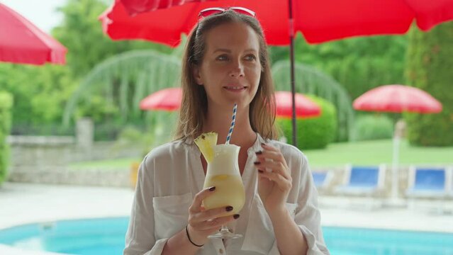 Woman drinking cocktail at poolside in summer. Relaxing vacation. Slow motion 4k video, copy space at end.