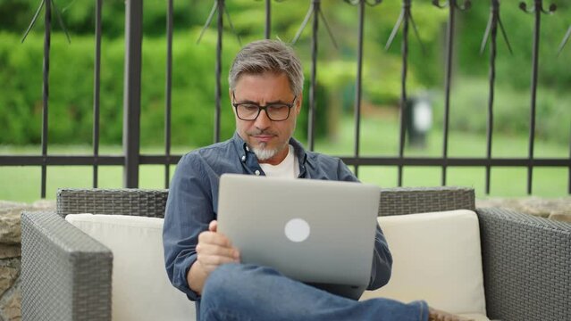 Man working with laptop computer outdoor, sitting in garden at home, . managing business online from home office. Portrait, happy confident smile.