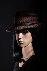 Plastic woman mannequin with brown hat posing for a low key film noir studio shoot on a black background