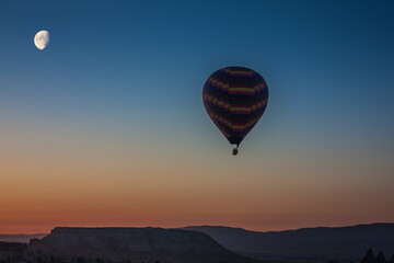 Hot air balloons flying over bizarre rock landscape in Cappadocia. Balloons fly early in the morning. Beautiful hot air balloons in the morning sky. Moon in the sky. Goreme. Turkey