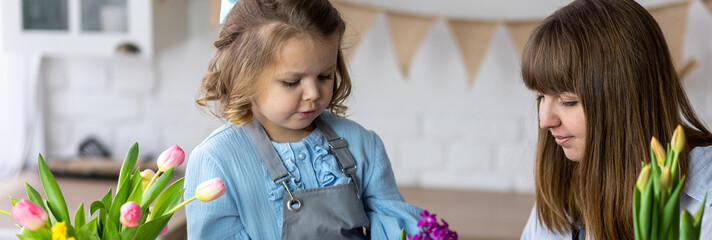 Happy mother and daughter doing home gardening together in the kitchen, taking care about flowers,...