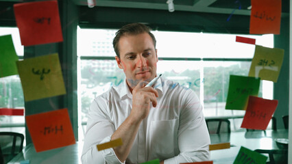Smart businessman thinking about start up project in front of glass board. Smiling male project...