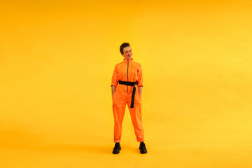 Obraz premium Full length body size photo of happy woman wear modern orange overalls on bright yellow color background. Cheerful and energetic middle age female with colored make up having fun near copy space