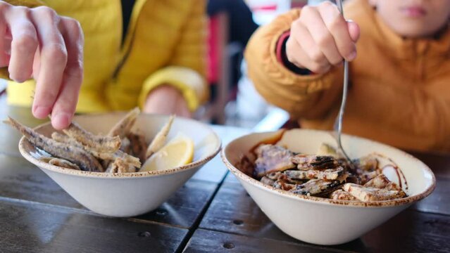 Family eating Spanish tapas on a terrace of a restaurant in Barcelona, patatas bravas, pescado frito and other typical tapas. Subjective point of view, hand and food, action.