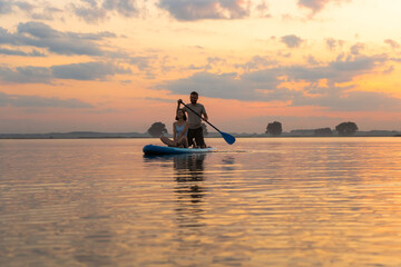 Happy couple paddle boarding at lake during sunset together. Concept of active family tourism and...