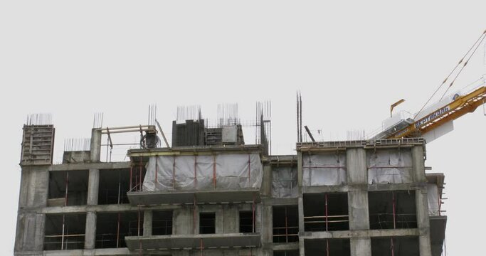 Jib of tall crane and people work on top of unfinished house