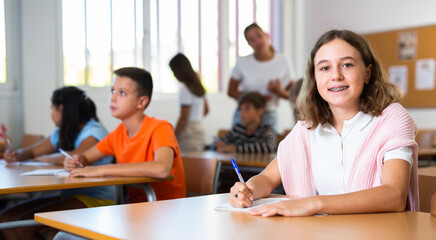 Girl sitting at desk in classroom and studying subjects during lesson in school.